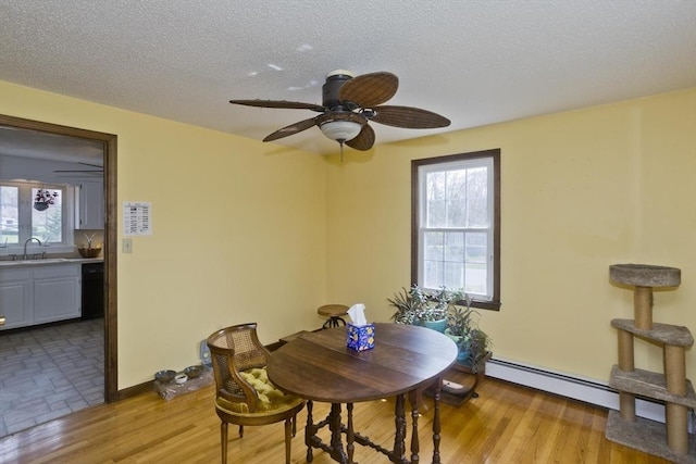 dining area with a textured ceiling, plenty of natural light, a baseboard heating unit, and ceiling fan