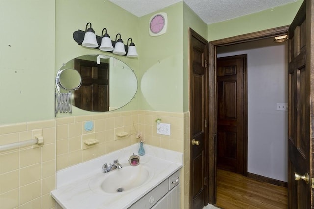 bathroom featuring vanity, wood finished floors, tile walls, a textured ceiling, and a wainscoted wall