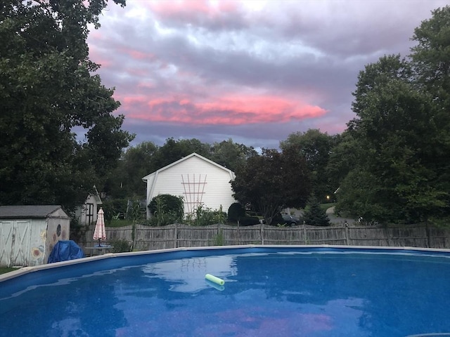 pool at dusk featuring an outdoor structure, fence, a storage shed, and a fenced in pool
