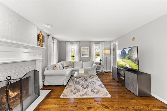 living room featuring a brick fireplace, dark wood-style flooring, and baseboards