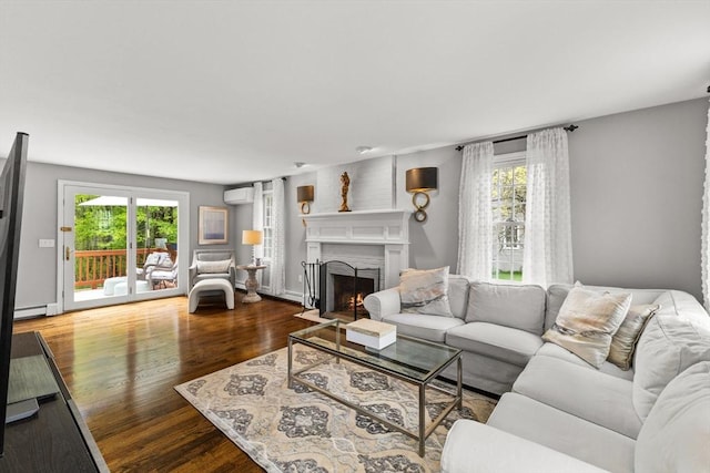 living area with a wall mounted air conditioner, healthy amount of natural light, a fireplace with flush hearth, and wood finished floors