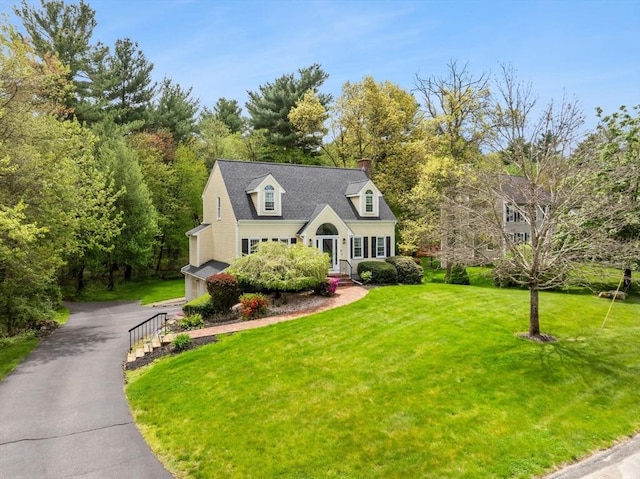 cape cod-style house featuring driveway, a front lawn, and a chimney