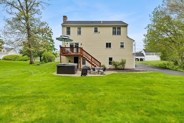 back of property featuring a hot tub, a chimney, a lawn, a wooden deck, and a patio area