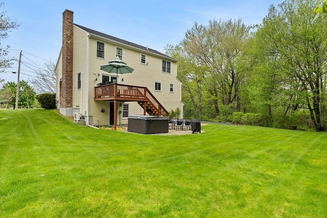 back of property with a hot tub, a chimney, a lawn, and a deck