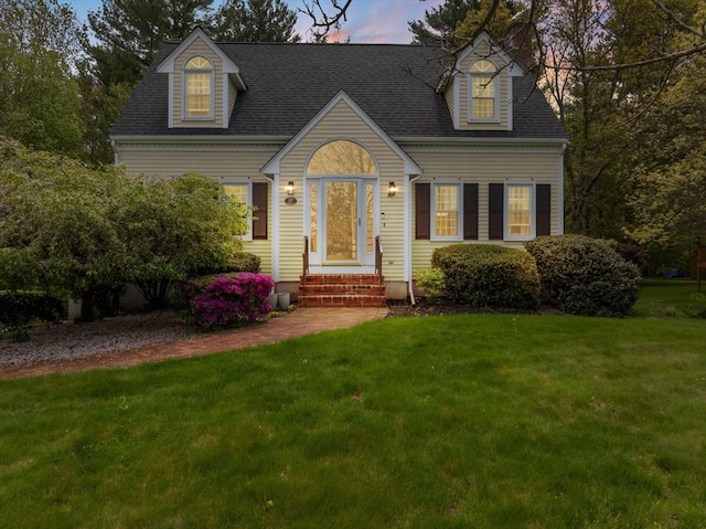 cape cod-style house with a lawn and roof with shingles