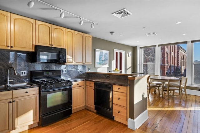 kitchen with black appliances, kitchen peninsula, sink, and light hardwood / wood-style flooring