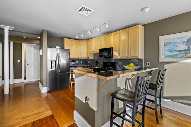 kitchen featuring black appliances, a kitchen breakfast bar, light brown cabinets, and kitchen peninsula