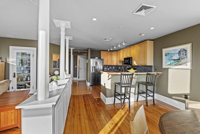 kitchen with kitchen peninsula, stainless steel fridge, light wood-type flooring, decorative columns, and light brown cabinets