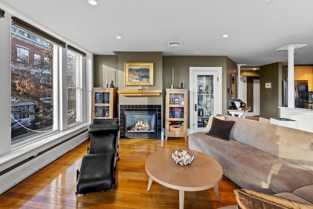 living room featuring a fireplace, light wood-type flooring, baseboard heating, and ornate columns