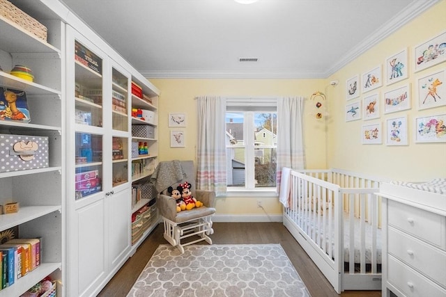 bedroom with ornamental molding, dark wood-type flooring, baseboards, and a crib