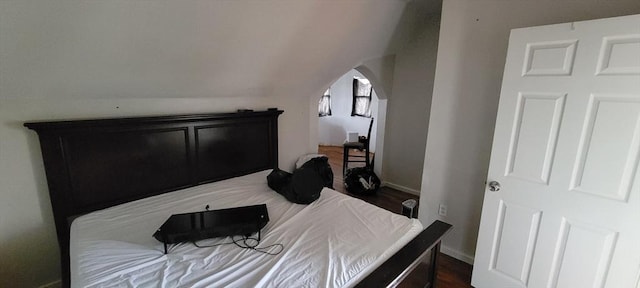 bedroom with lofted ceiling, baseboards, arched walkways, and dark wood-type flooring