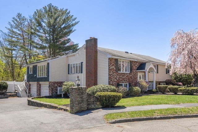 bi-level home featuring an attached garage, driveway, a front lawn, and a chimney