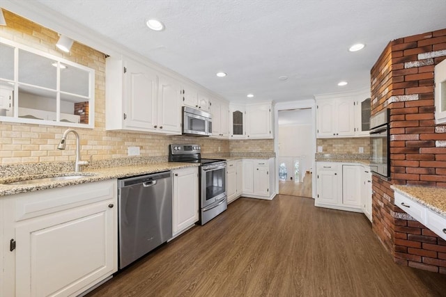 kitchen with stainless steel appliances, a sink, dark wood-type flooring, white cabinets, and tasteful backsplash