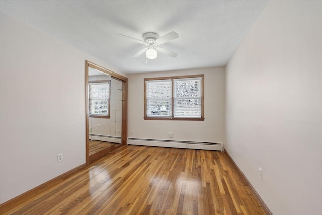 empty room with baseboard heating, a ceiling fan, wood finished floors, and baseboards