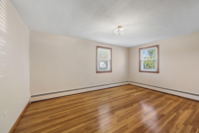 spare room featuring wood finished floors, a baseboard heating unit, and baseboards