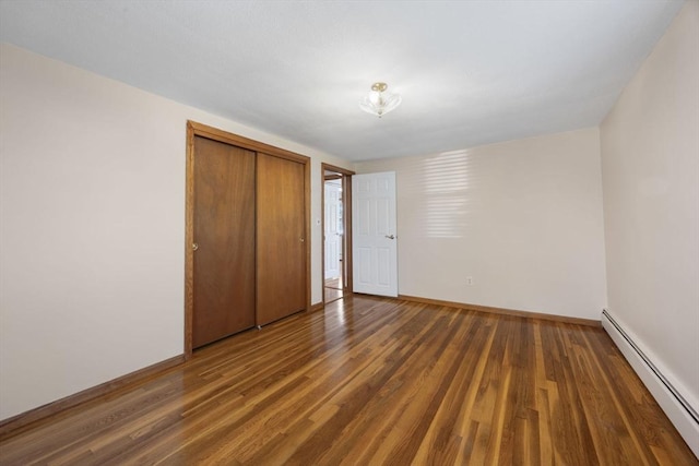 unfurnished bedroom with a baseboard heating unit, wood finished floors, baseboards, and a closet