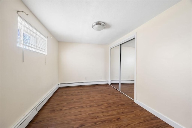unfurnished bedroom with a baseboard heating unit, a closet, wood finished floors, and baseboards