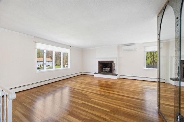 unfurnished living room with a baseboard radiator, a brick fireplace, a wall unit AC, wood finished floors, and crown molding