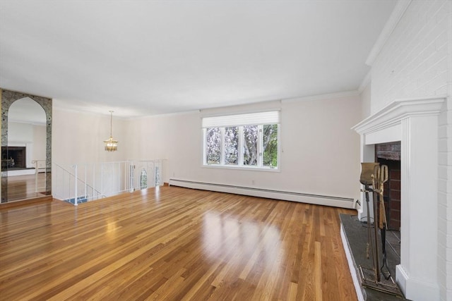 unfurnished living room featuring a fireplace, a baseboard heating unit, wood finished floors, crown molding, and arched walkways
