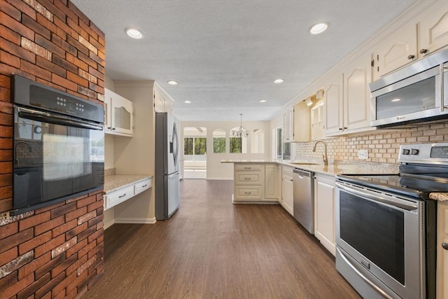 kitchen featuring stainless steel appliances, a peninsula, a sink, backsplash, and dark wood-style flooring