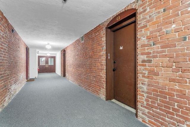 hallway with brick wall, light colored carpet, and a textured ceiling