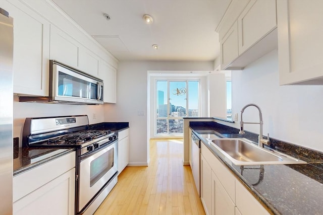 kitchen featuring appliances with stainless steel finishes, sink, dark stone countertops, light hardwood / wood-style floors, and white cabinetry