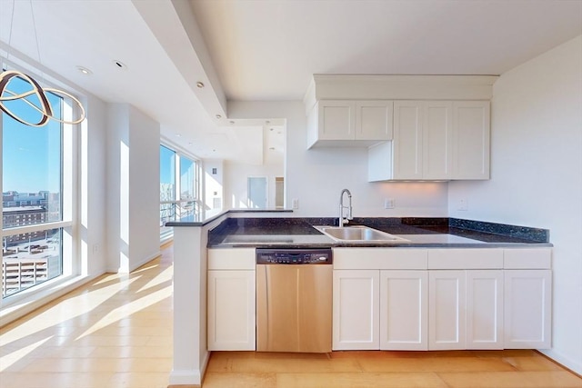 kitchen with dark stone counters, white cabinets, sink, stainless steel dishwasher, and light wood-type flooring