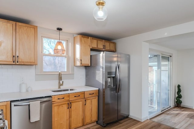 kitchen featuring appliances with stainless steel finishes, decorative light fixtures, sink, decorative backsplash, and light wood-type flooring