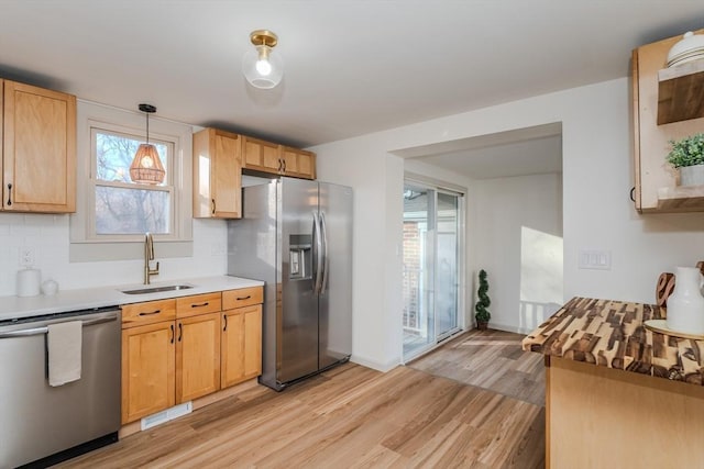 kitchen featuring appliances with stainless steel finishes, pendant lighting, tasteful backsplash, sink, and light hardwood / wood-style floors