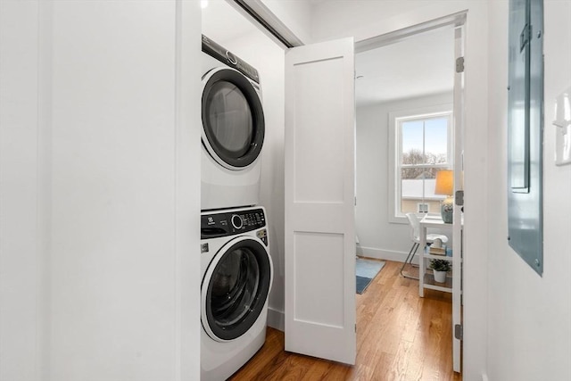 clothes washing area with wood-type flooring and stacked washer / drying machine