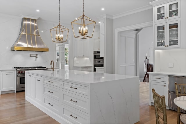 kitchen featuring island exhaust hood, a center island with sink, light stone countertops, stainless steel appliances, and decorative light fixtures