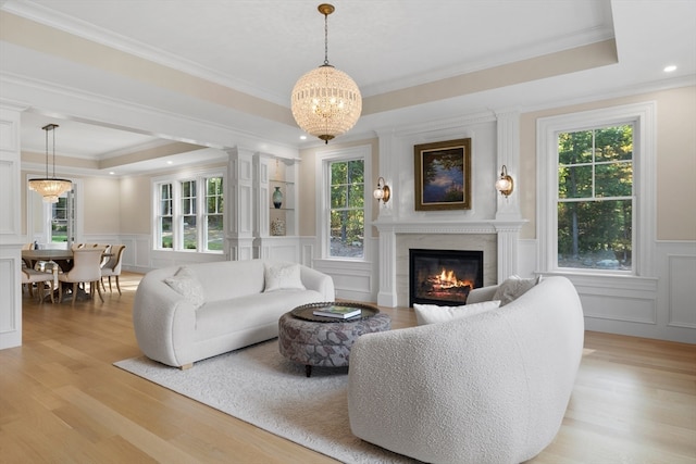 living room with ornamental molding, a fireplace, a tray ceiling, and light hardwood / wood-style floors