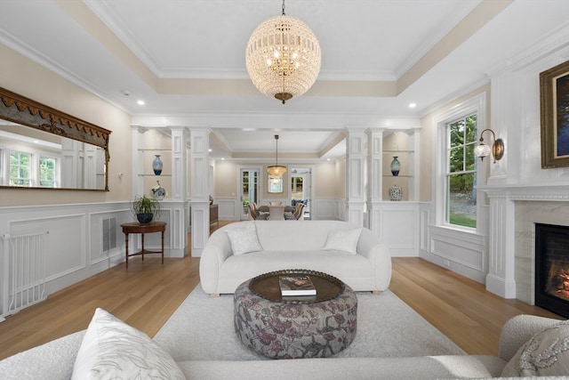 living room featuring ornate columns, ornamental molding, a tray ceiling, and light wood-type flooring