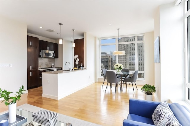 kitchen featuring dark brown cabinetry, light wood-style floors, a peninsula, stainless steel microwave, and decorative backsplash