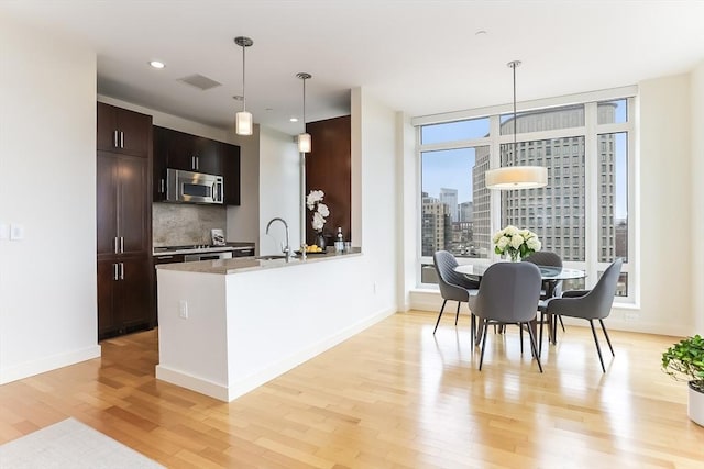 kitchen featuring dark brown cabinetry, a sink, stainless steel microwave, light wood-type flooring, and tasteful backsplash