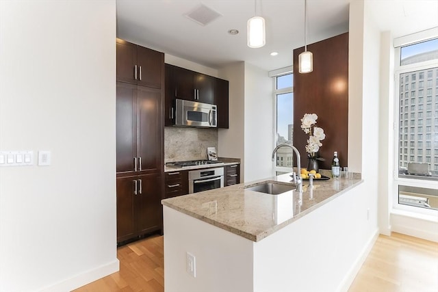 kitchen with baseboards, light wood-type flooring, tasteful backsplash, a sink, and stainless steel appliances