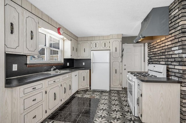 kitchen featuring white appliances, dark countertops, a textured ceiling, premium range hood, and a sink