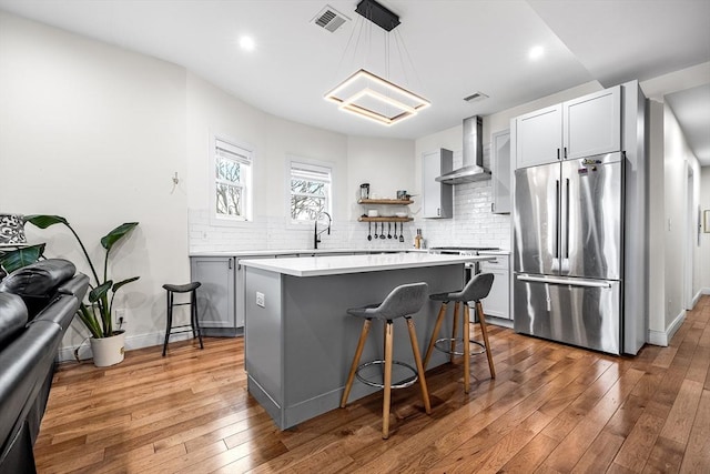 kitchen featuring tasteful backsplash, visible vents, hardwood / wood-style floors, appliances with stainless steel finishes, and wall chimney exhaust hood