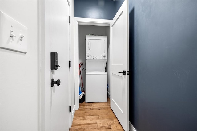 clothes washing area featuring light wood-style floors, laundry area, and stacked washer / dryer