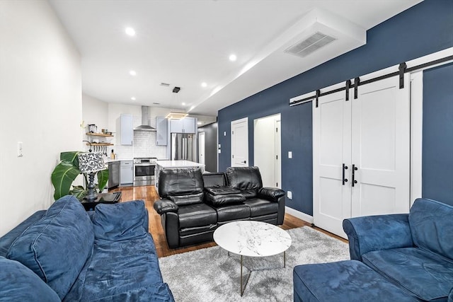 living area with a barn door, recessed lighting, wood finished floors, and visible vents