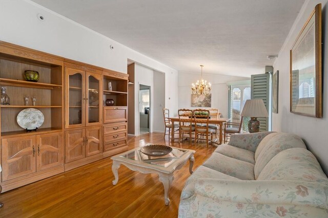living room with a chandelier, light wood-style floors, and vaulted ceiling