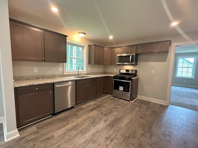 kitchen featuring baseboards, appliances with stainless steel finishes, light stone counters, wood finished floors, and a sink