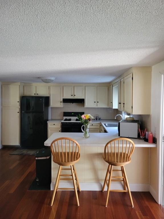 115 Captain Chase Rd, Yarmouth, MA 02664 - kitchen with black appliances, a textured ceiling, a peninsula, dark wood-style flooring, and under cabinet range hood