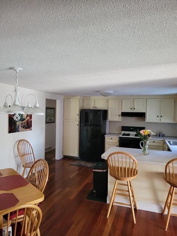 115 Captain Chase Rd, Yarmouth, MA 02664 - kitchen featuring black appliances, under cabinet range hood, a textured ceiling, dark wood-style flooring, and a peninsula