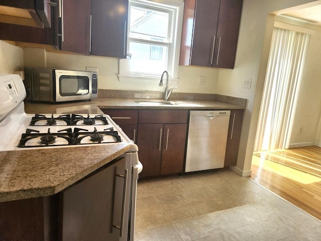 kitchen with a sink, appliances with stainless steel finishes, baseboards, and dark brown cabinets