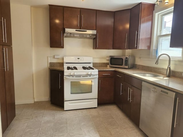 kitchen with light stone countertops, dark brown cabinets, a sink, under cabinet range hood, and stainless steel appliances