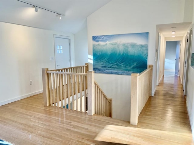 corridor with light hardwood / wood-style flooring, rail lighting, and lofted ceiling