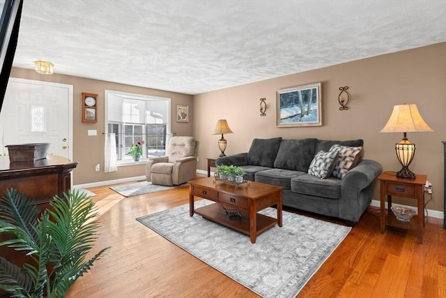 living room with a textured ceiling, baseboards, and light wood-style floors