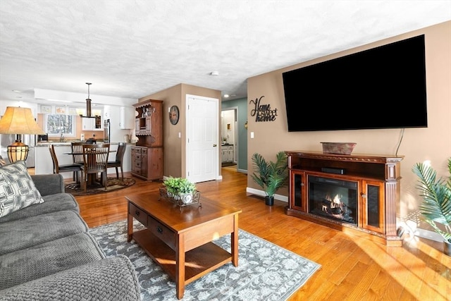 living area featuring a textured ceiling, baseboards, wood finished floors, and a glass covered fireplace