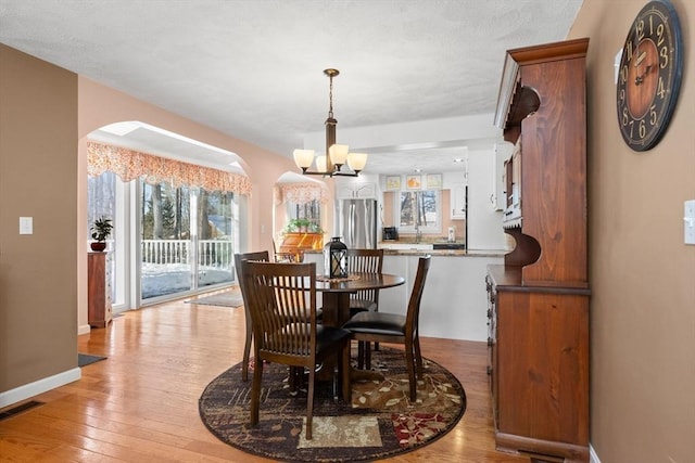 dining area featuring light wood finished floors, visible vents, baseboards, arched walkways, and a notable chandelier